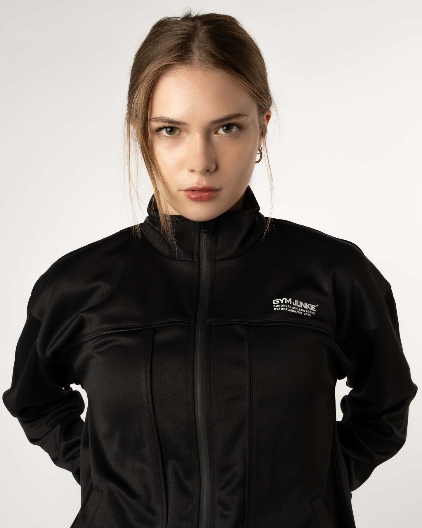 Close-up van vrouwelijke model in GJA Classic Track Jacket, details van stof en design, moderne en krachtige sportkleding voor jonge vrouwen in Nederland - Gym Junkie dames sportkleing