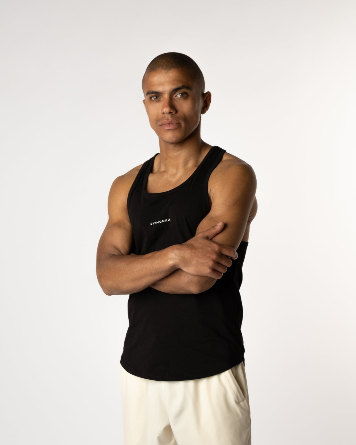 Semi zijaanzicht van een mannelijk model met gevouwen armen in de Magna Stringer uit de Gym Junkie  gymkleding collectie - Heren Sport tanktops