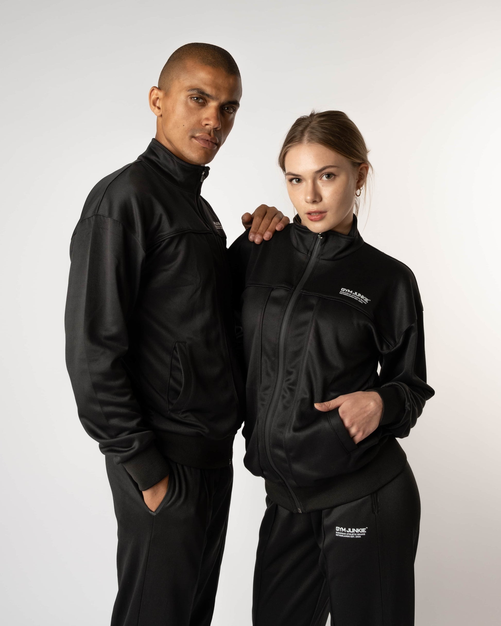 Man en vrouw dragen GJA trainingspakken, stoere en comfortabele sportoutfits voor jonge, zelfverzekerde sporters die grenzen verleggen in Nederland - Gym Junkie sportkleding voor heren en dames