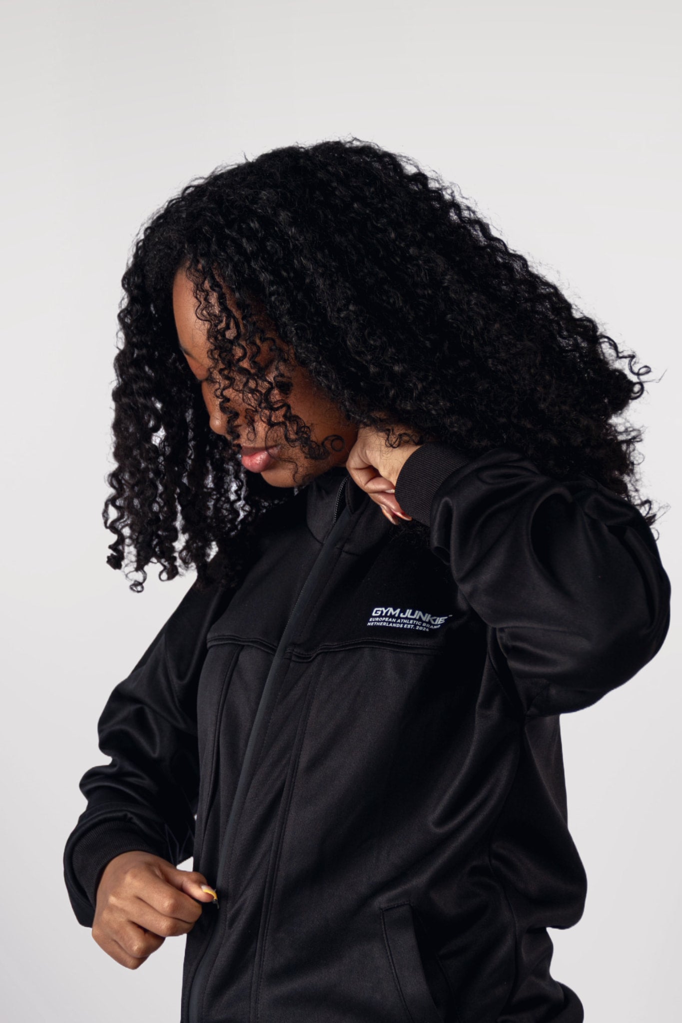Model die de rits van de GJA Classic Track Jacket dichtdoet, voor jonge vrouwen die met stijl en attitude de sportschool veroveren in Nederland - Gym Junkie Sportskleding voor dames