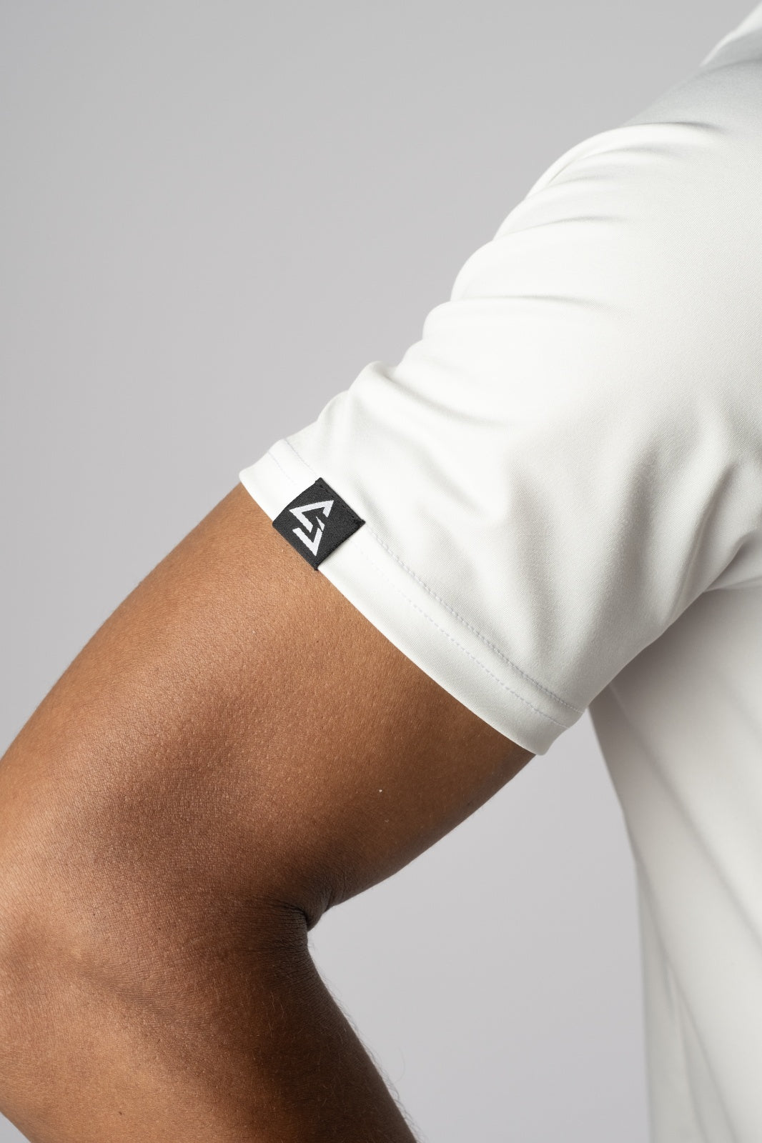 Close-up van het Gym Junkie-label op de mouw van de witte Magna Tee, minimalistisch design met oog voor detail