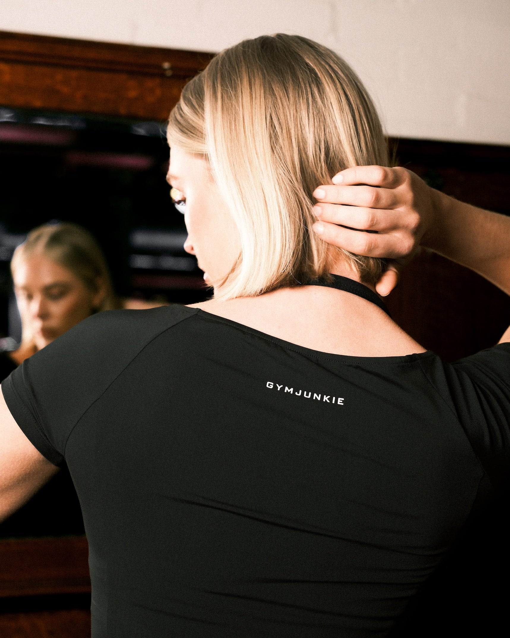 Dame houdt haar haar omhoog – achteraanzicht van de Nora boat neck T-shirt in Charcoal Black met zichtbaar gedrukt logo