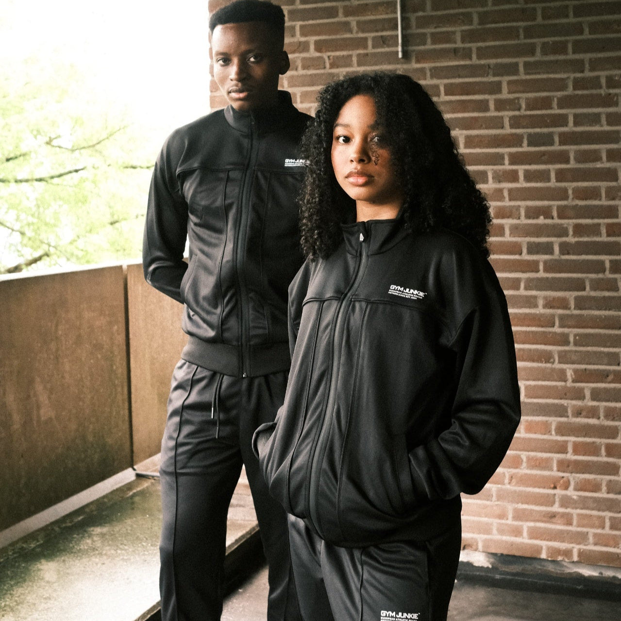 Man en vrouw dragen het GJA Classic Trainingspak buiten – stijlvolle lifestylefoto voor actieve jongeren