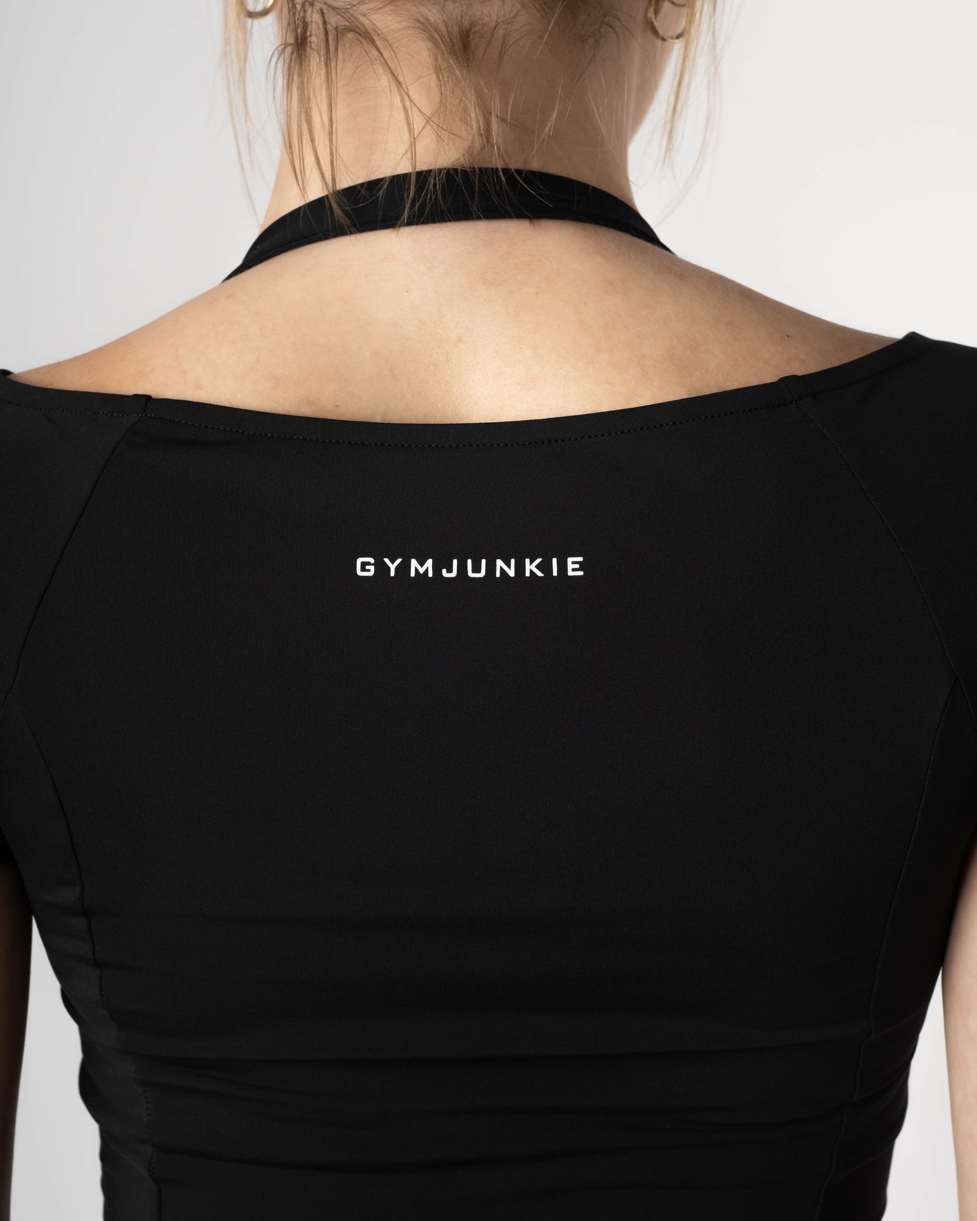 Close-up van de achterkant van de Nora Boothals Crop Top in Charcoal Black, gedragen door een vrouw, Gym Junkie. - Sporttops voor dames