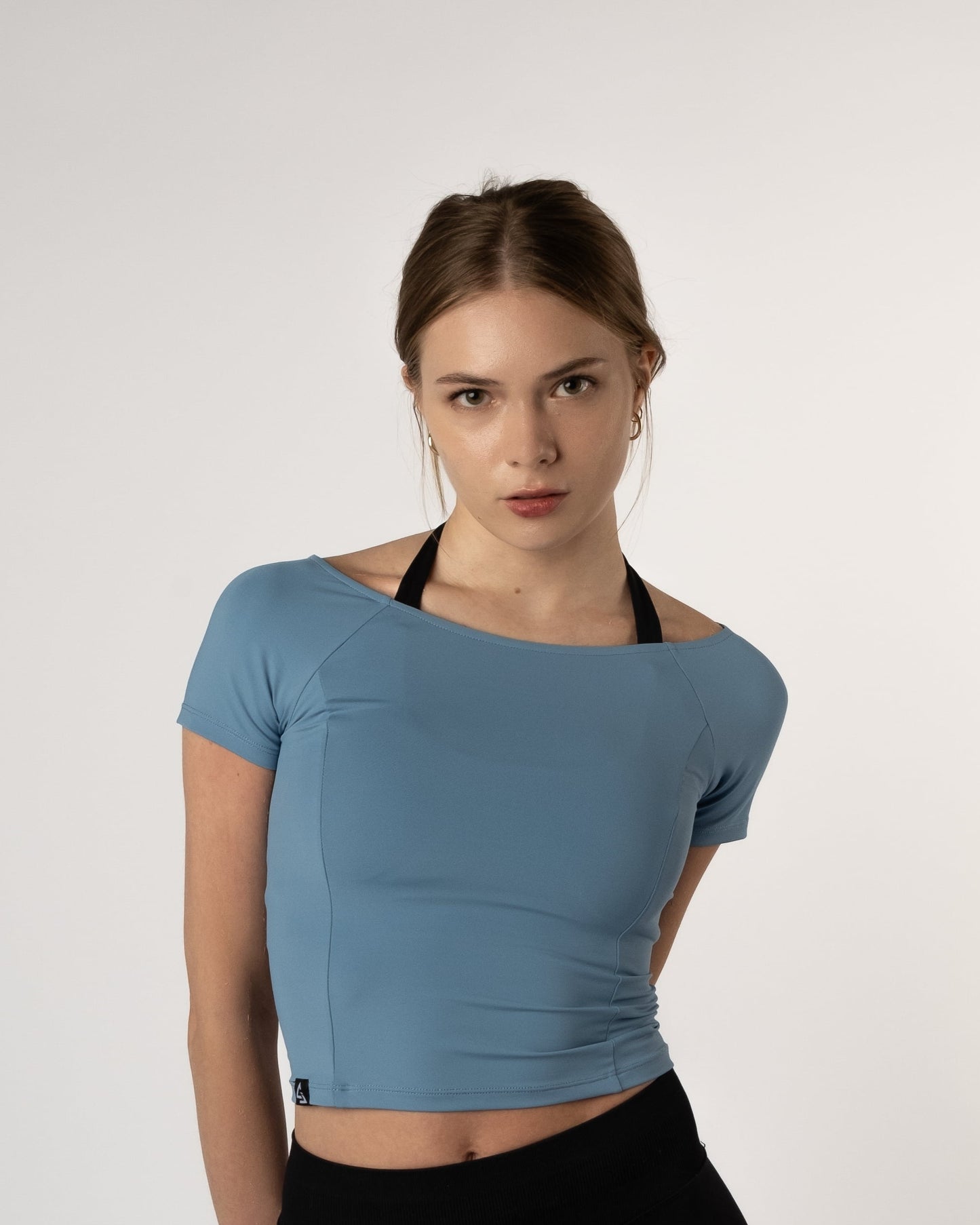 Vrouw draagt de Nora Boothals Crop Top in lichtblauw van Gym Junkie met haar armen achter haar rug.