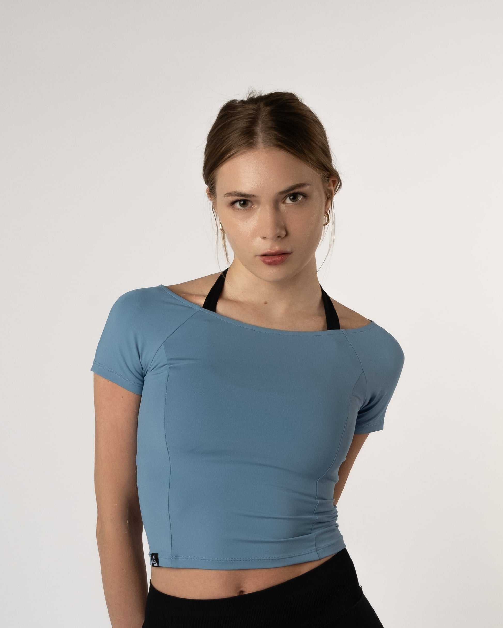 Vrouw draagt de Nora Boothals Crop Top in lichtblauw van Gym Junkie met haar armen achter haar rug.